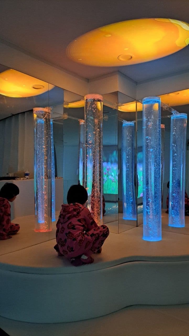 이용자가 버블튜브 앞에 앉아 색이 변하는 물방울 조명을 바라보는 모습